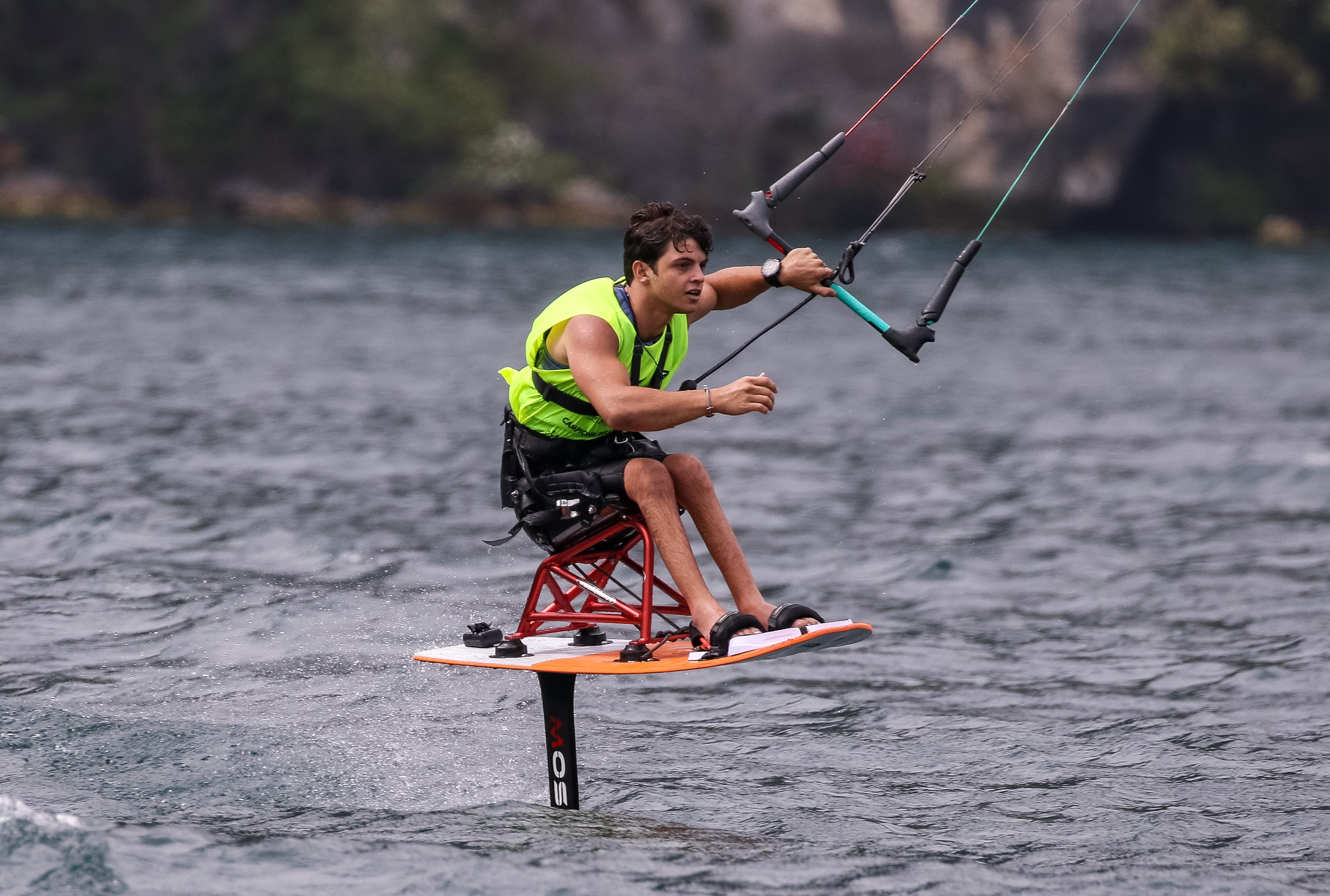 Un jeune homme paraplégique est en train de faire du kite surf. Il se tient sur sa planche en position assise grâce à un châssis vissé sur la planche.